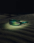 MAESTRALE — green shield visor sunglasses still life on dark dune sand