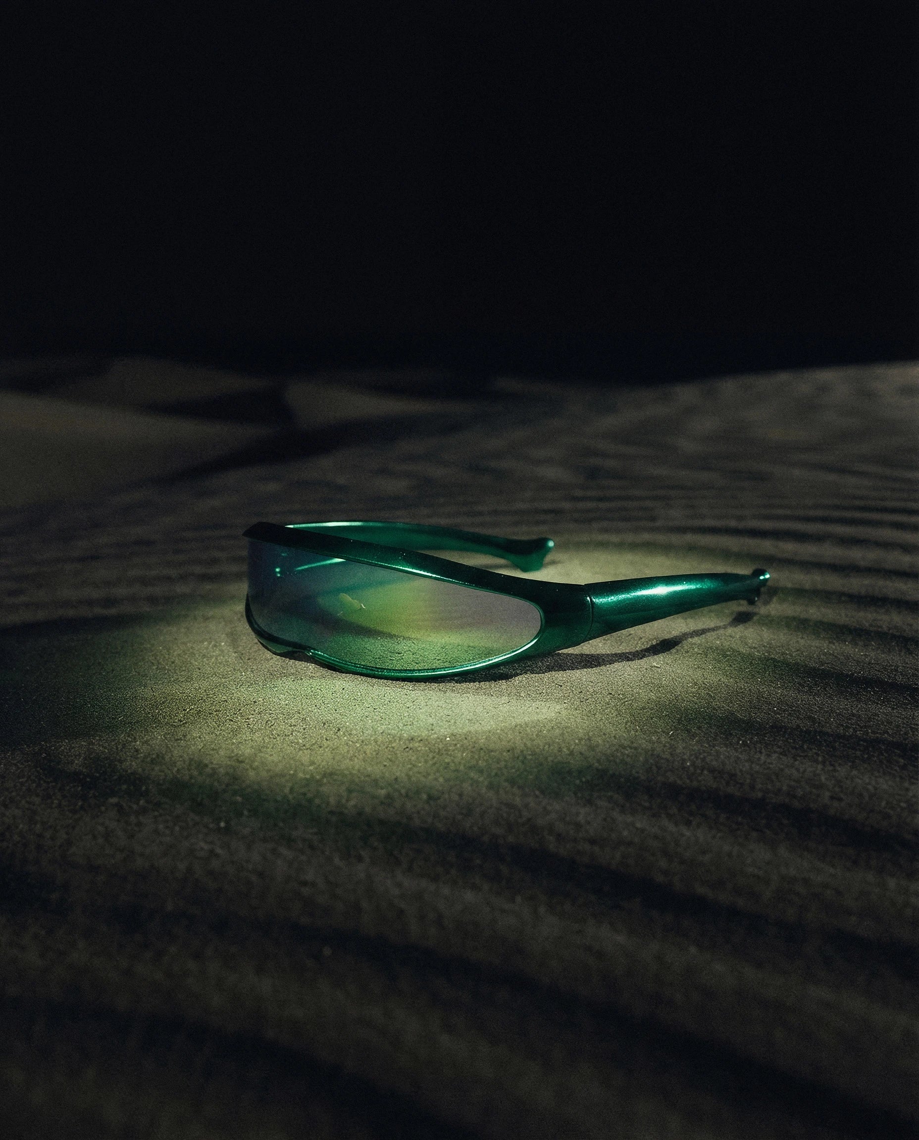 MAESTRALE — green shield visor sunglasses still life on dark dune sand