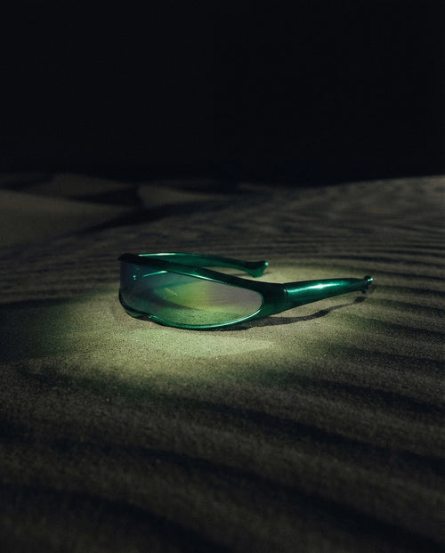 MAESTRALE — green shield visor sunglasses still life on dark dune sand